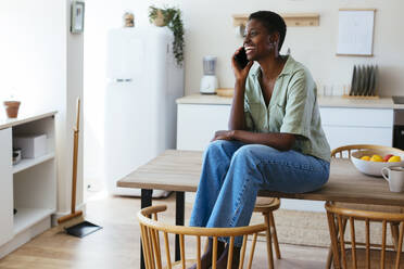 Happy young woman talking on smart phone in kitchen at home - EBSF03465