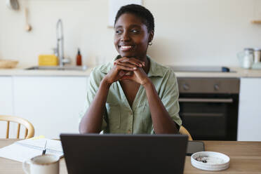 Smiling freelancer with hand on chin sitting at table - EBSF03467