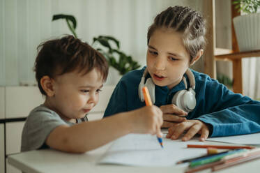 Brother teaching sibling to draw on paper at home - ANAF01464