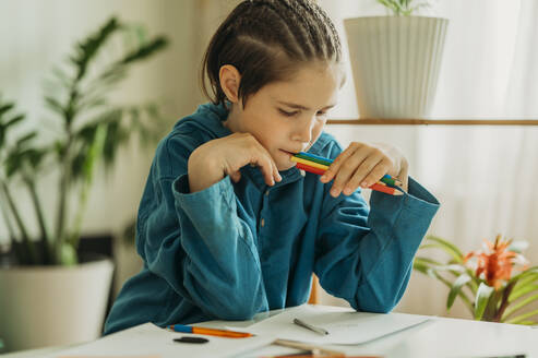Thoughtful boy holding colored pencils at home - ANAF01467