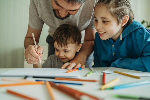 Lächelnder Vater bringt seinen Söhnen zu Hause das Zeichnen mit Bleistift bei - ANAF01469