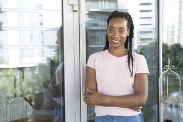 Smiling woman with arms crossed leaning on glass wall - SVKF01404