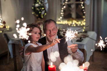 Portrait of senior grandfather with small granddaughter indoors at Christmas, having fun with sparklers. - HPIF18754