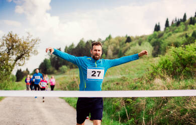 Ein männlicher Läufer beim Überqueren der Ziellinie in einem Wettlauf in der Natur. - HPIF18774