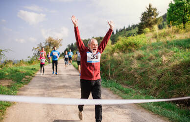 Ein älterer männlicher Läufer beim Überqueren der Ziellinie in einem Wettlauf in der Natur. - HPIF18781