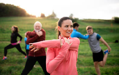 Vorderansicht einer großen Gruppe fitter und aktiver Menschen, die sich nach einer Übung in der Natur dehnen. - HPIF18810
