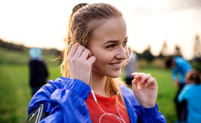 A portrait of young woman with earphones resting after doing exercise in nature. - HPIF18824