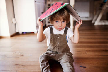 Ein kleiner Junge spielt zu Hause mit großen Spielzeugfrüchten und schaut in die Kamera. - HPIF18908