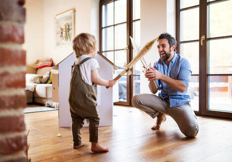 A toddler boy and father with carton swords playing indoors at home, fighting. - HPIF18936