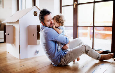 Zwei glückliche Kleinkinder mit einem Vater und einem Haus aus Pappe spielen zu Hause. - HPIF18939