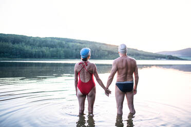 Rückansicht eines älteren Paares im Badeanzug, das vor dem Schwimmen im Freien am See steht. - HPIF18965