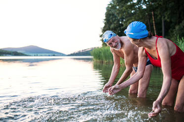 Älteres Paar im Badeanzug, das vor dem Schwimmen im See steht, Kopierraum. - HPIF18967