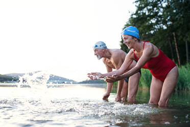 Älteres Paar im Badeanzug, das vor dem Schwimmen im See steht, Kopierraum. - HPIF18968