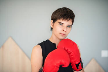 Front view of young woman with red boxing gloves standing indoors at home. - HPIF18983