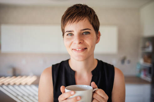 A front view of young woman with coffee standing indoors at home. - HPIF18987