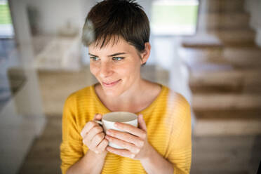 Vorderansicht einer jungen Frau mit Kaffee, die zu Hause steht, Aufnahme durch Glas. - HPIF19010