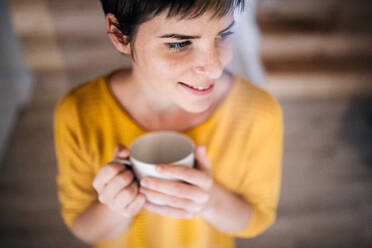 Vorderansicht einer jungen Frau mit Kaffee, die zu Hause steht, Aufnahme durch Glas. - HPIF19011