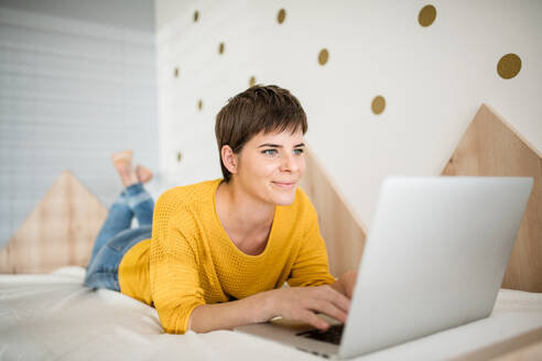 Eine junge Frau mit Laptop liegt auf dem Bett im Schlafzimmer zu Hause. - HPIF19026