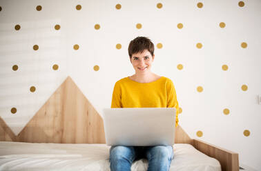 Vorderansicht einer jungen Frau mit Laptop auf dem Bett im Schlafzimmer zu Hause. - HPIF19029