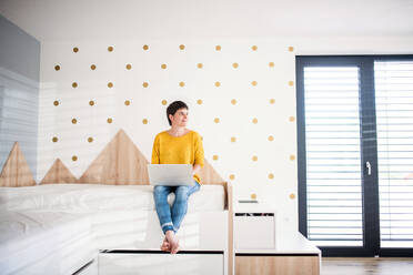 Vorderansicht einer jungen Frau mit Laptop auf dem Bett im Schlafzimmer zu Hause. - HPIF19033