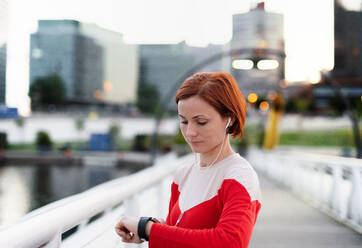 A young woman with smartwatch on bridge outdoors in city, resting after exercise. - HPIF19135