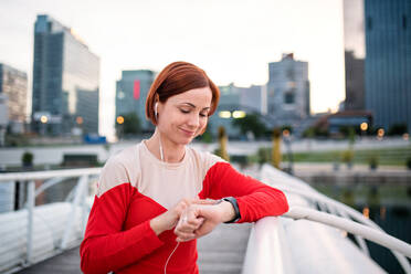 Junge Läuferin mit Kopfhörern in der Stadt, die beim Ausruhen eine Smartwatch benutzt. - HPIF19141