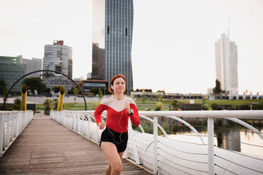 Front view of young woman runner with earphones jogging outdoors in city. - HPIF19142