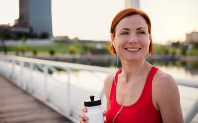 Young woman runner with water bottle in city, resting on the bridge. Copy space. - HPIF19150