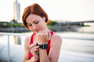 Young woman runner with earphones in city, using smartwatch when resting. - HPIF19156