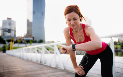 Young woman runner with earphones in city, using smartwatch when resting. - HPIF19157