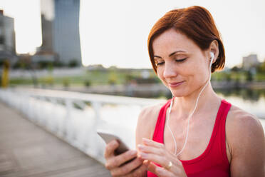 Young woman runner with earphones in city, using smartphone when resting. - HPIF19159