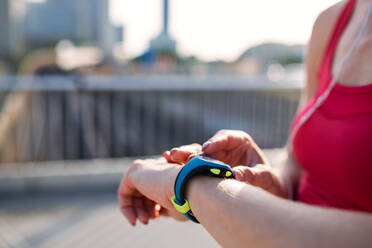 Midsection of young woman with smartwatch outdoors in city, resting after exercise. - HPIF19190