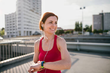 Young woman runner with earphones in city, using smartwatch when resting. - HPIF19191