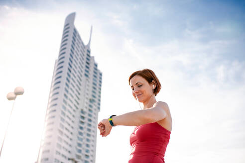 Niedriger Blickwinkel auf eine junge Frau mit Smartwatch in der Stadt, die sich nach dem Sport ausruht. - HPIF19192