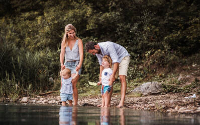 Eine junge Familie mit zwei Kleinkindern, die im Sommer draußen am Fluss mit Papierbooten spielen. - HPIF19227
