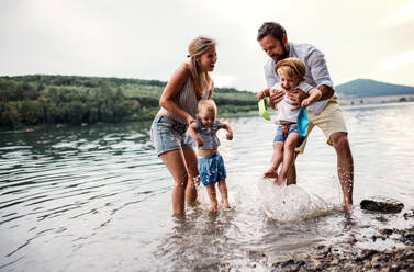Eine junge Familie mit zwei Kleinkindern, die sich im Sommer draußen am Fluss vergnügen. - HPIF19228