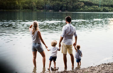 A rear view of young family with two toddler children spending time outdoors by the river in summer. - HPIF19232