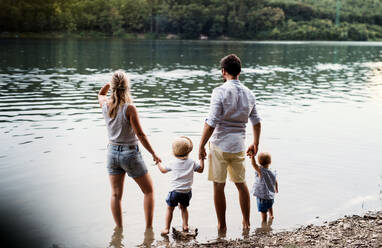 Rückansicht einer jungen Familie mit zwei Kleinkindern, die im Sommer ihre Zeit im Freien am Fluss verbringen. - HPIF19232