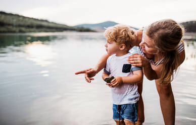 A young mother with a toddler boy outdoors by the river in summer. Copy space. - HPIF19242