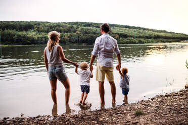 Rückansicht einer jungen Familie mit zwei Kleinkindern, die im Sommer ihre Zeit im Freien am Fluss verbringen. - HPIF19259