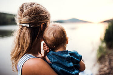 A rear view of mother with a toddler daughter standing outdoors by the river in summer. - HPIF19272