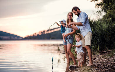 Eine junge Familie mit zwei Kleinkindern, die im Sommer draußen am Fluss mit Papierbooten spielen. - HPIF19275