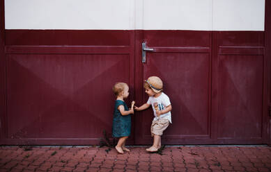 Two small toddler children outdoors in summer, eating ice cream and standing in front of a gate. - HPIF19286