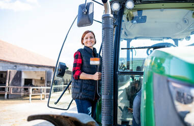 Arbeiterin steht an einem Traktor auf einem Milchviehbetrieb und schaut in die Kamera, Landwirtschaft. - HPIF19381