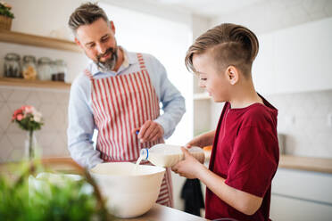 Ein reifer Vater mit seinem kleinen Sohn in der Küche, der Pfannkuchen macht. - HPIF19405