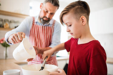 Ein reifer Vater mit seinem kleinen Sohn in der Küche, der Pfannkuchen macht. - HPIF19406