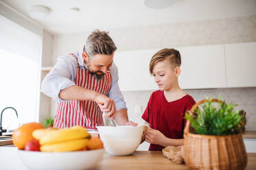 Ein reifer Vater mit seinem kleinen Sohn in der Küche, der Pfannkuchen macht. - HPIF19408