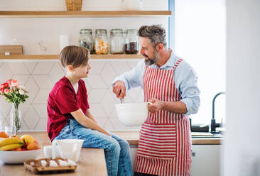 A mature father with small son indoors in kitchen, making pancakes. - HPIF19409