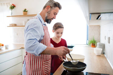 Ein reifer Vater mit seinem kleinen Sohn in der Küche, der Pfannkuchen macht. - HPIF19410