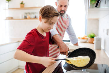 Ein kleiner Junge mit seinem Vater in der Küche, der lernt, wie man Pfannkuchen macht. - HPIF19414